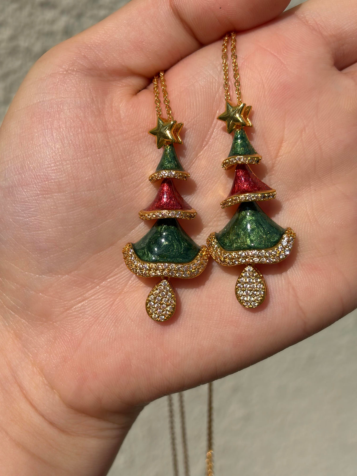 Two Christmas tree necklaces with green and red enamel tiers, gold star and crystal pavé, shown in hand