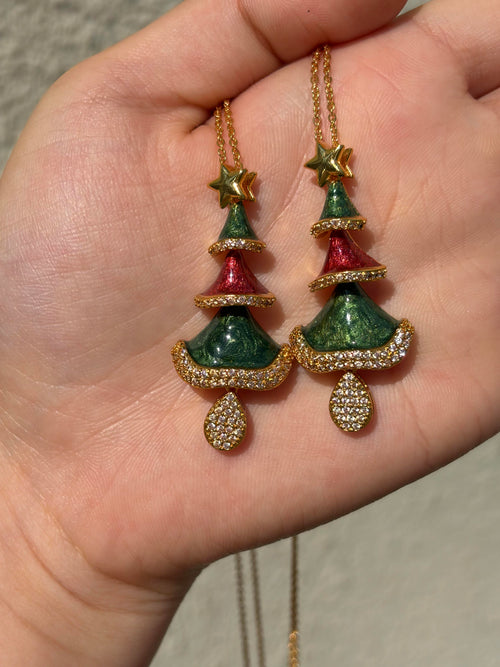 Two Christmas tree necklaces with green and red enamel tiers, gold star and crystal pavé, shown in hand