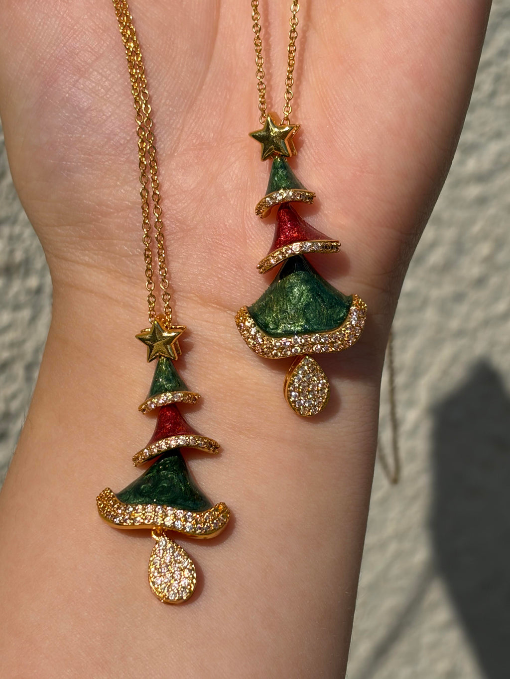 Gold-tone Christmas tree pendant necklaces with green and red enamel and sparkling crystals, held against the wrist