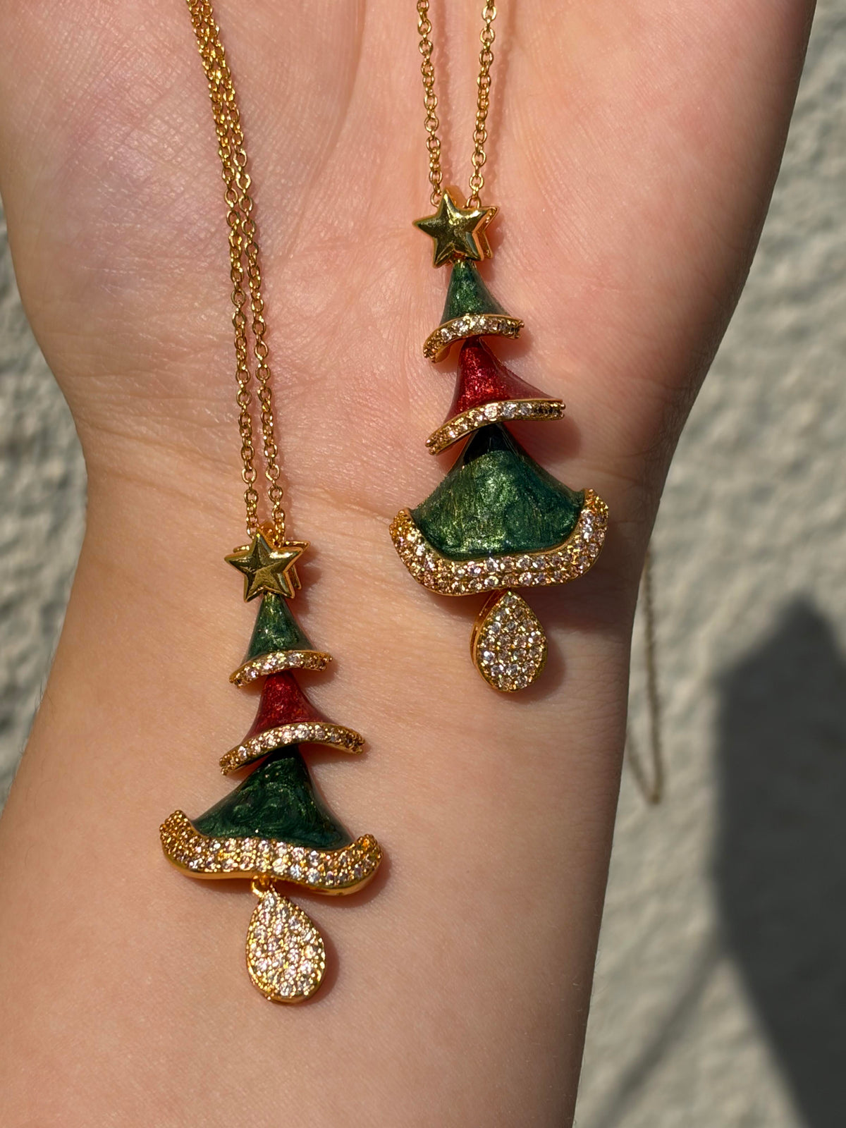 Gold-tone Christmas tree pendant necklaces with green and red enamel and sparkling crystals, held against the wrist